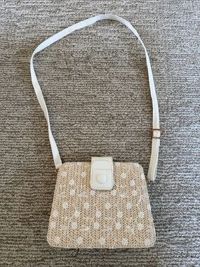 Woven straw crossbody bag featuring a white floral embroidery overlay